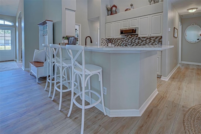 kitchen featuring decorative backsplash, a breakfast bar, sink, white cabinets, and light hardwood / wood-style floors