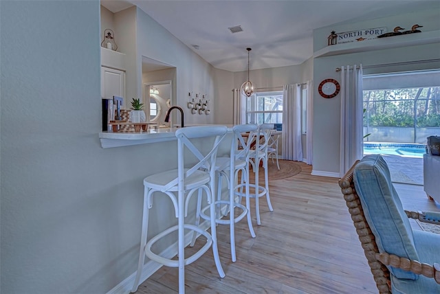 kitchen with kitchen peninsula, vaulted ceiling, light hardwood / wood-style flooring, a chandelier, and hanging light fixtures