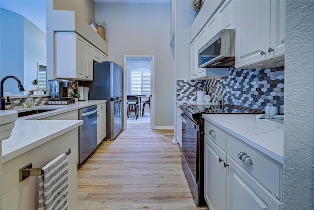 kitchen with sink, appliances with stainless steel finishes, light hardwood / wood-style floors, light stone counters, and white cabinetry