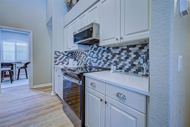 kitchen with electric range oven, light stone counters, light hardwood / wood-style flooring, decorative backsplash, and white cabinets