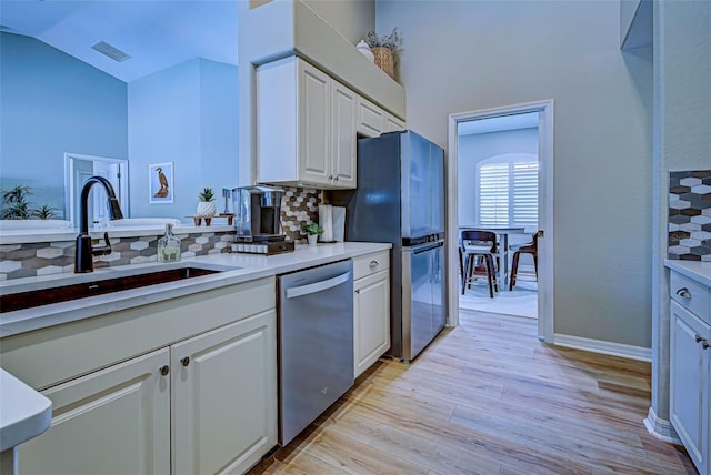 kitchen with white cabinetry, sink, stainless steel appliances, tasteful backsplash, and light hardwood / wood-style flooring