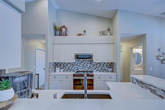 kitchen featuring decorative backsplash, appliances with stainless steel finishes, white cabinetry, and lofted ceiling