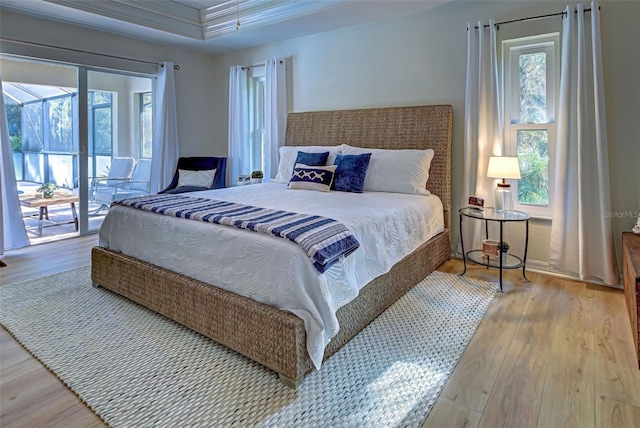 bedroom featuring access to exterior, hardwood / wood-style floors, a raised ceiling, and ornamental molding