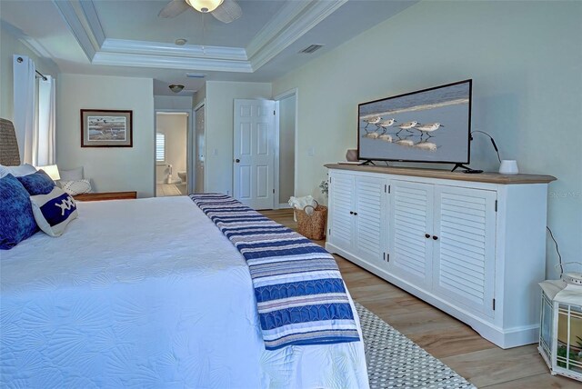 bedroom featuring a raised ceiling, ensuite bath, ceiling fan, light wood-type flooring, and ornamental molding