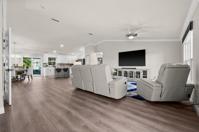 living room featuring ceiling fan with notable chandelier, light hardwood / wood-style floors, and crown molding