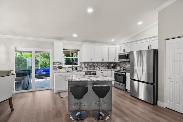 kitchen featuring stainless steel appliances, light stone countertops, white cabinets, and vaulted ceiling