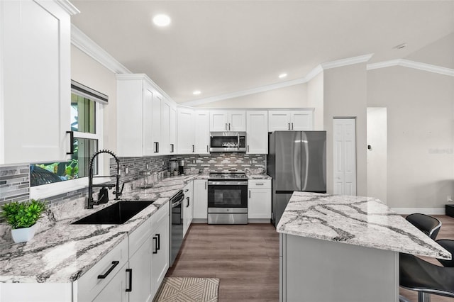 kitchen with stainless steel appliances, sink, vaulted ceiling, a kitchen breakfast bar, and white cabinets