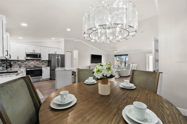 dining area with dark wood-type flooring, an inviting chandelier, vaulted ceiling, and ornamental molding