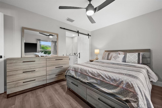 bedroom featuring hardwood / wood-style floors, a barn door, and ceiling fan