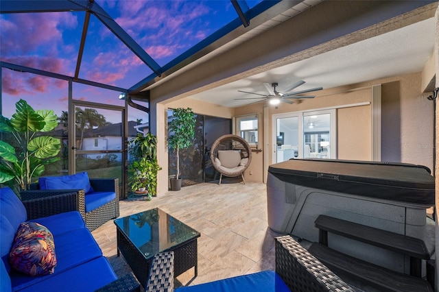 patio terrace at dusk featuring a lanai, outdoor lounge area, ceiling fan, and a hot tub