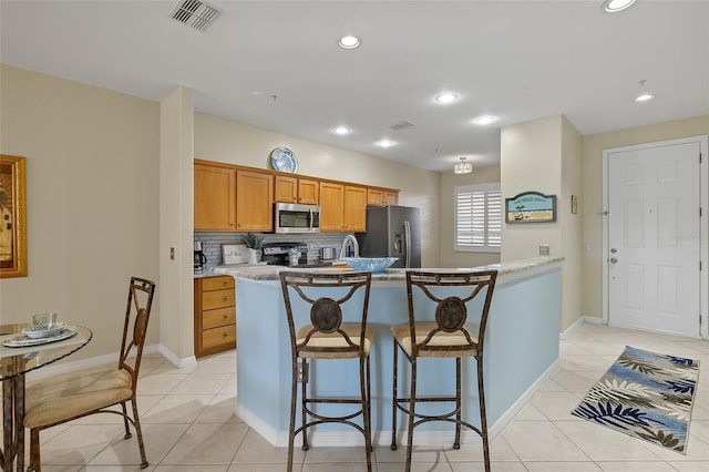 kitchen featuring a kitchen breakfast bar, light tile patterned flooring, appliances with stainless steel finishes, and tasteful backsplash