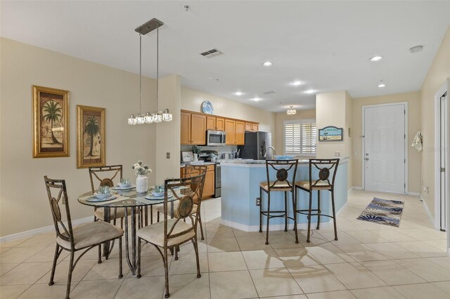 kitchen featuring stainless steel appliances, hanging light fixtures, light tile patterned floors, a kitchen island with sink, and a kitchen breakfast bar