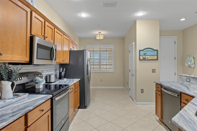 kitchen with decorative backsplash, appliances with stainless steel finishes, light tile patterned floors, and light stone countertops