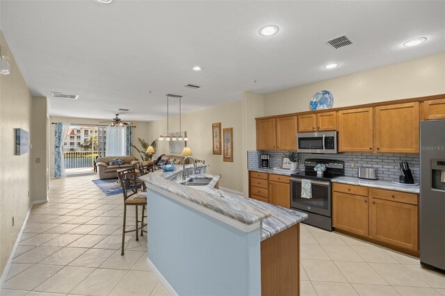 kitchen with sink, a kitchen island with sink, light tile patterned flooring, backsplash, and appliances with stainless steel finishes