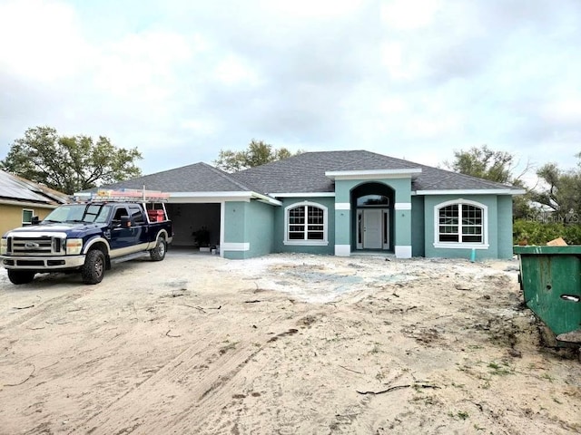 ranch-style home featuring driveway, a shingled roof, an attached garage, and stucco siding