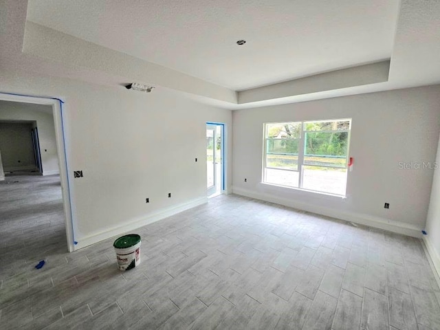 spare room featuring baseboards, a tray ceiling, and wood finish floors