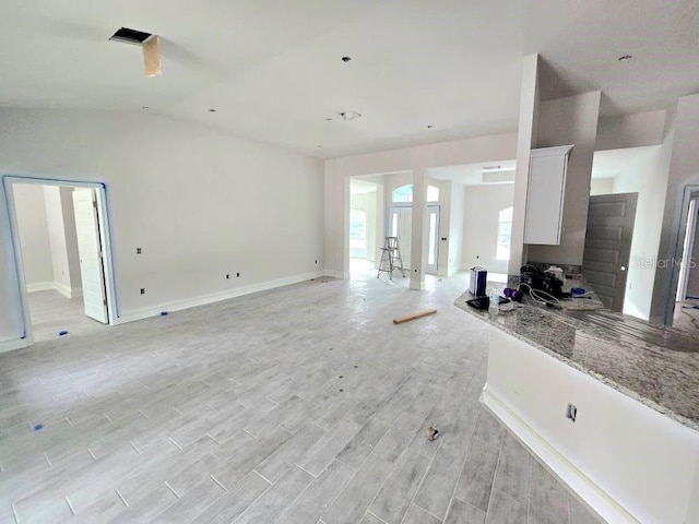 unfurnished living room with light wood-style flooring, baseboards, and vaulted ceiling