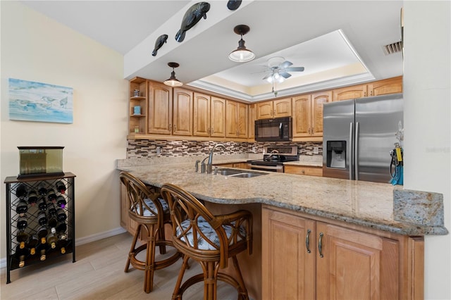 kitchen featuring appliances with stainless steel finishes, a raised ceiling, light stone countertops, sink, and kitchen peninsula