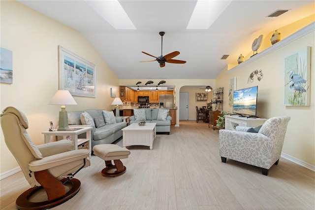 living room featuring light wood-type flooring, ceiling fan, and vaulted ceiling with skylight