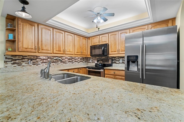 kitchen with a tray ceiling, appliances with stainless steel finishes, sink, and light stone counters