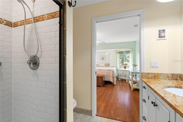 bathroom with hardwood / wood-style floors, vanity, toilet, and a tile shower