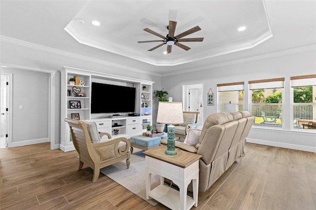 living room with ceiling fan, ornamental molding, light wood-type flooring, and a tray ceiling