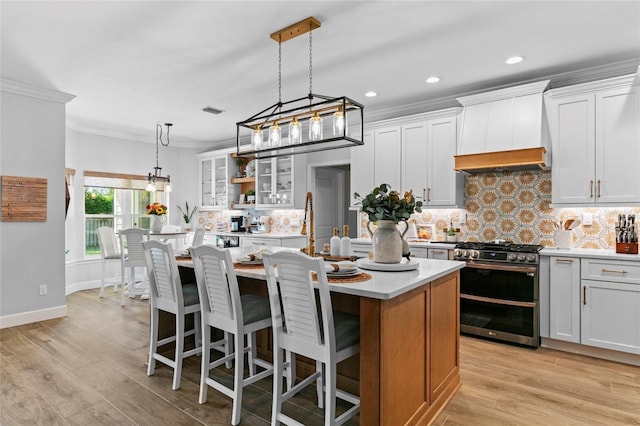 kitchen with white cabinetry, stainless steel range with gas stovetop, decorative light fixtures, and an island with sink