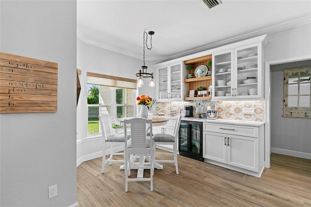 kitchen with hanging light fixtures, white cabinetry, wine cooler, and light hardwood / wood-style flooring