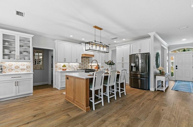 kitchen with white cabinets, dark hardwood / wood-style flooring, a center island with sink, and stainless steel fridge with ice dispenser