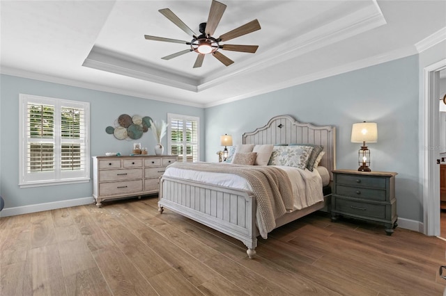 bedroom featuring light hardwood / wood-style floors, a raised ceiling, multiple windows, and ceiling fan