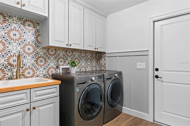 clothes washing area with light hardwood / wood-style flooring, cabinets, sink, and washer and dryer