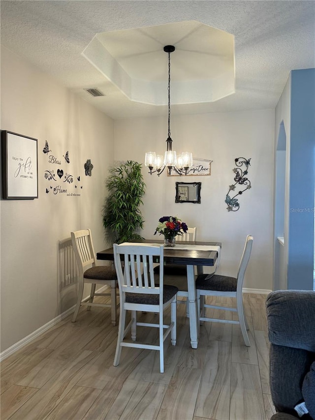5101 Pine Shadow Ln, North Port, FL 34287 - dining area featuring a textured ceiling, a chandelier, a tray ceiling, light wood-style floors, and baseboards