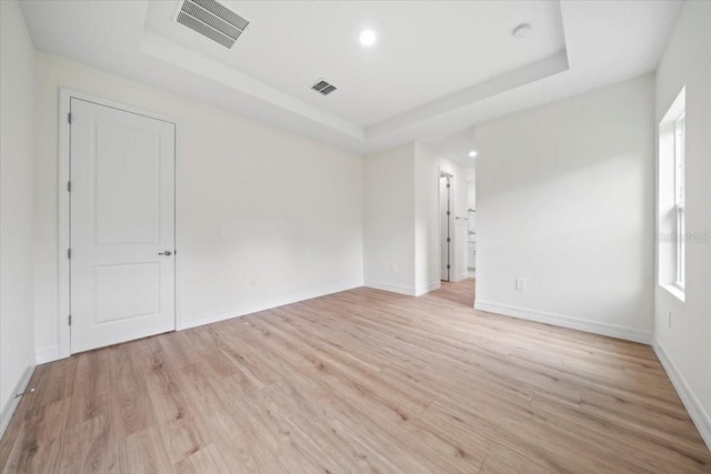 spare room featuring a tray ceiling, a wealth of natural light, and light wood-type flooring