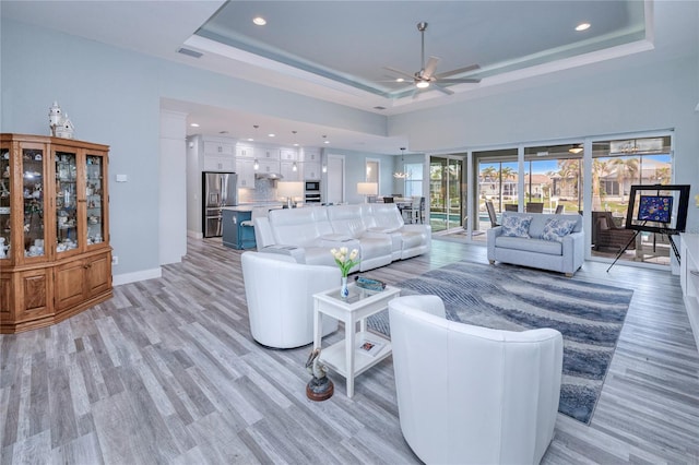 living room featuring light hardwood / wood-style flooring, ceiling fan, and a tray ceiling