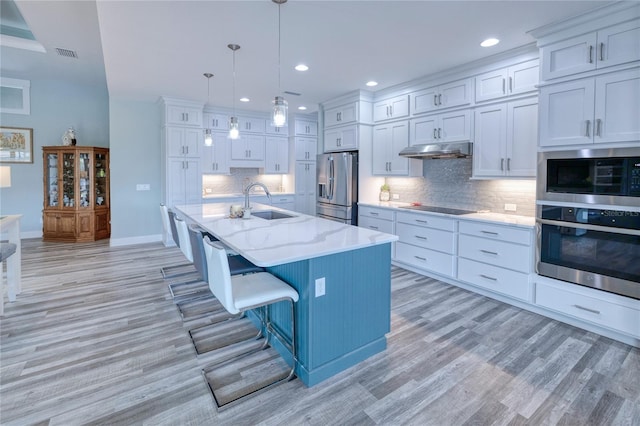 kitchen with a kitchen bar, appliances with stainless steel finishes, a center island with sink, light hardwood / wood-style flooring, and hanging light fixtures