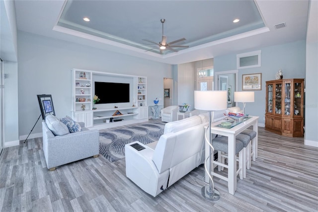 living room featuring built in shelves, a tray ceiling, ceiling fan, and light hardwood / wood-style floors