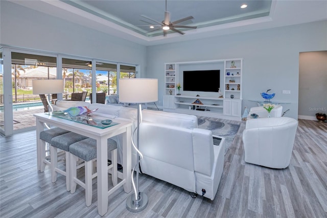 living room featuring light hardwood / wood-style floors, a raised ceiling, and ceiling fan