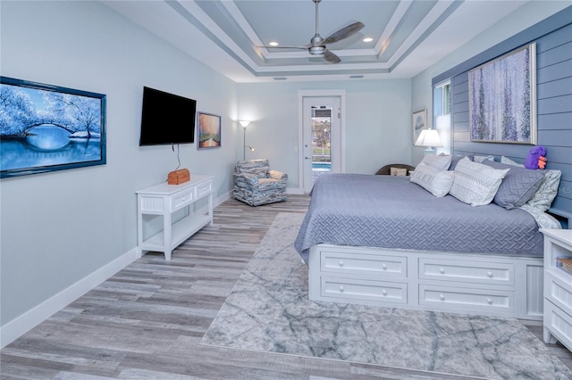 bedroom with ceiling fan, a raised ceiling, and light hardwood / wood-style floors