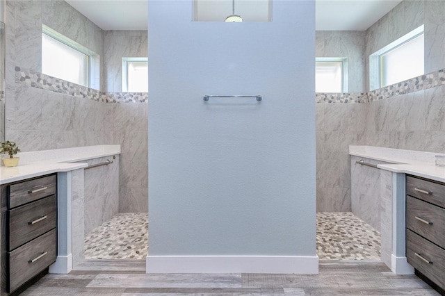 bathroom with hardwood / wood-style floors, vanity, a tile shower, and tile walls