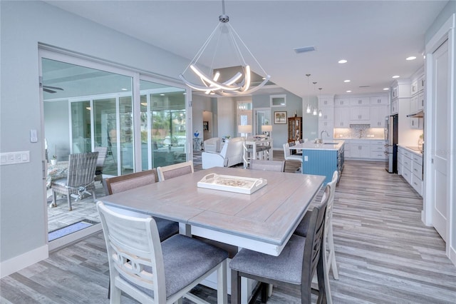 dining space featuring sink, light hardwood / wood-style floors, and ceiling fan with notable chandelier