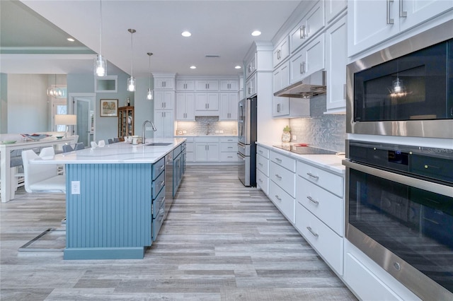 kitchen featuring stainless steel appliances, a kitchen island with sink, white cabinets, hanging light fixtures, and a breakfast bar area