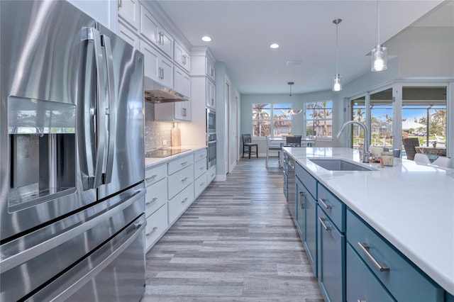 kitchen with appliances with stainless steel finishes, light wood-type flooring, sink, white cabinetry, and hanging light fixtures