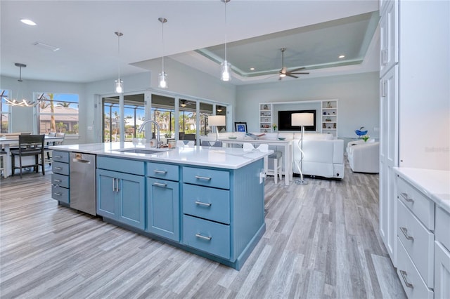 kitchen with light wood-type flooring, decorative light fixtures, a raised ceiling, and an island with sink