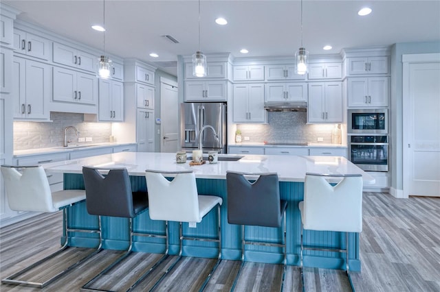 kitchen featuring hanging light fixtures, stainless steel appliances, a large island with sink, hardwood / wood-style floors, and a kitchen bar