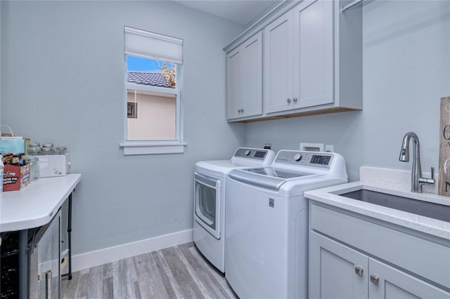 laundry area with cabinets, light hardwood / wood-style flooring, washer and clothes dryer, and sink