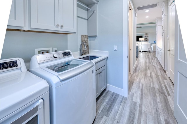 washroom with sink, light hardwood / wood-style flooring, cabinets, and independent washer and dryer