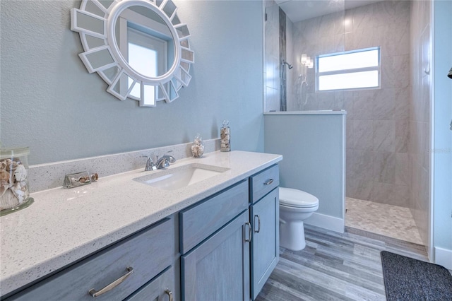 bathroom featuring toilet, hardwood / wood-style floors, vanity, and tiled shower