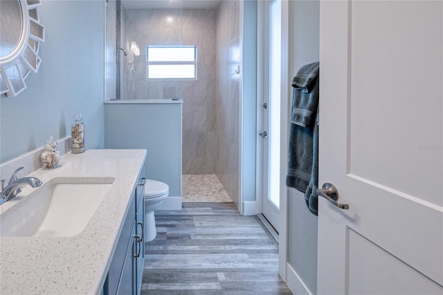 bathroom with a tile shower, vanity, wood-type flooring, and toilet