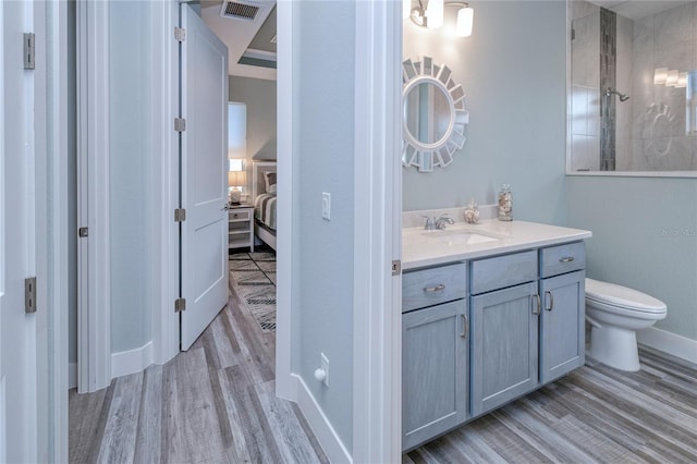 bathroom featuring toilet, wood-type flooring, vanity, and a tile shower