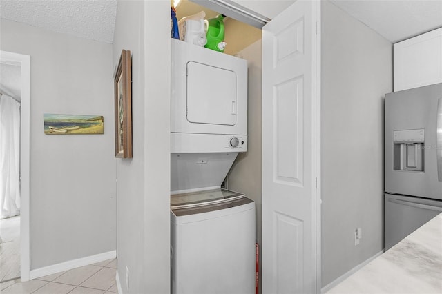 laundry room featuring stacked washer / drying machine, a textured ceiling, and light tile patterned flooring